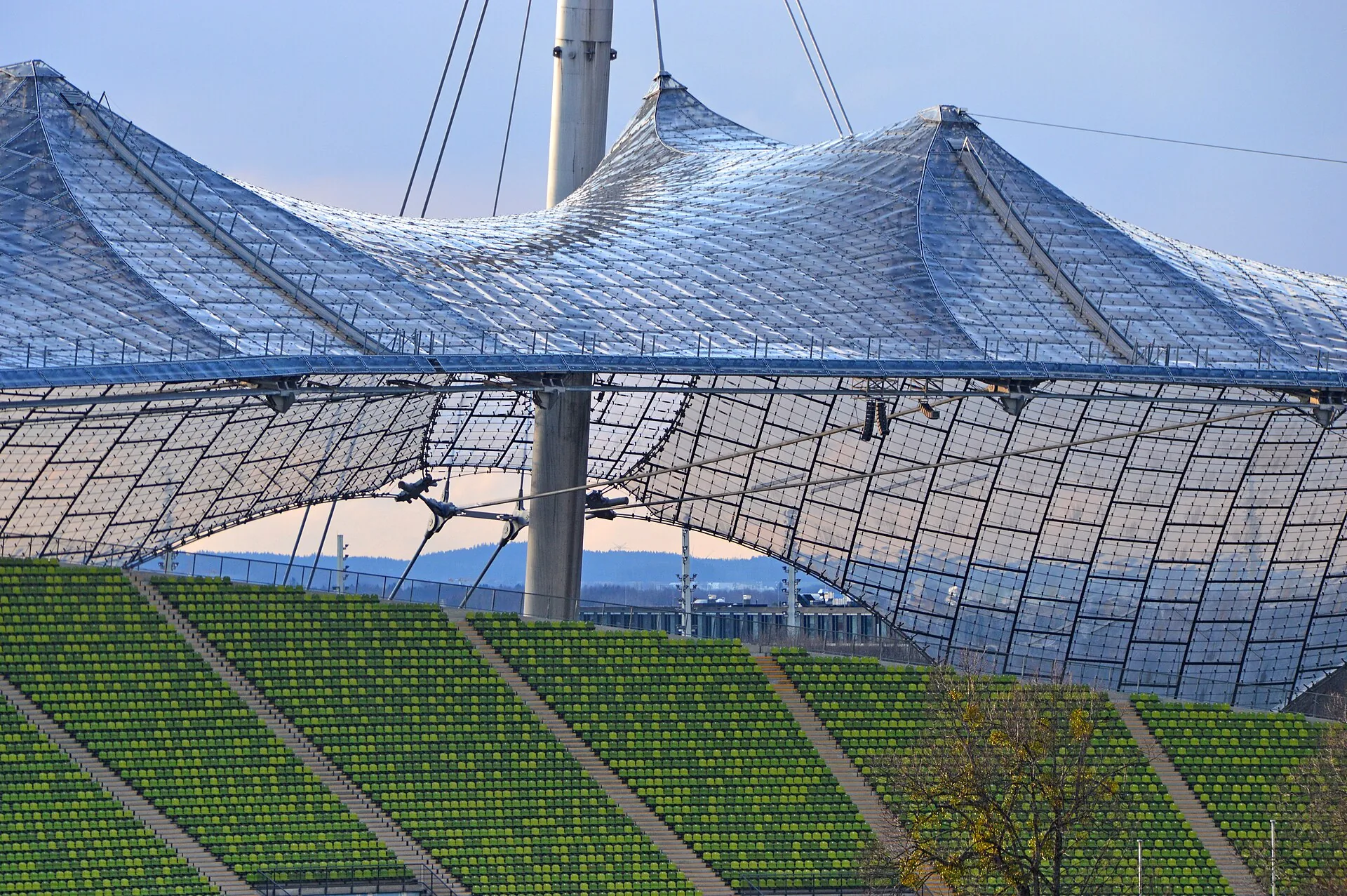 Translucent tent-like cable-net roof on tall masts above green stadium seating in Munich's Olympic Park