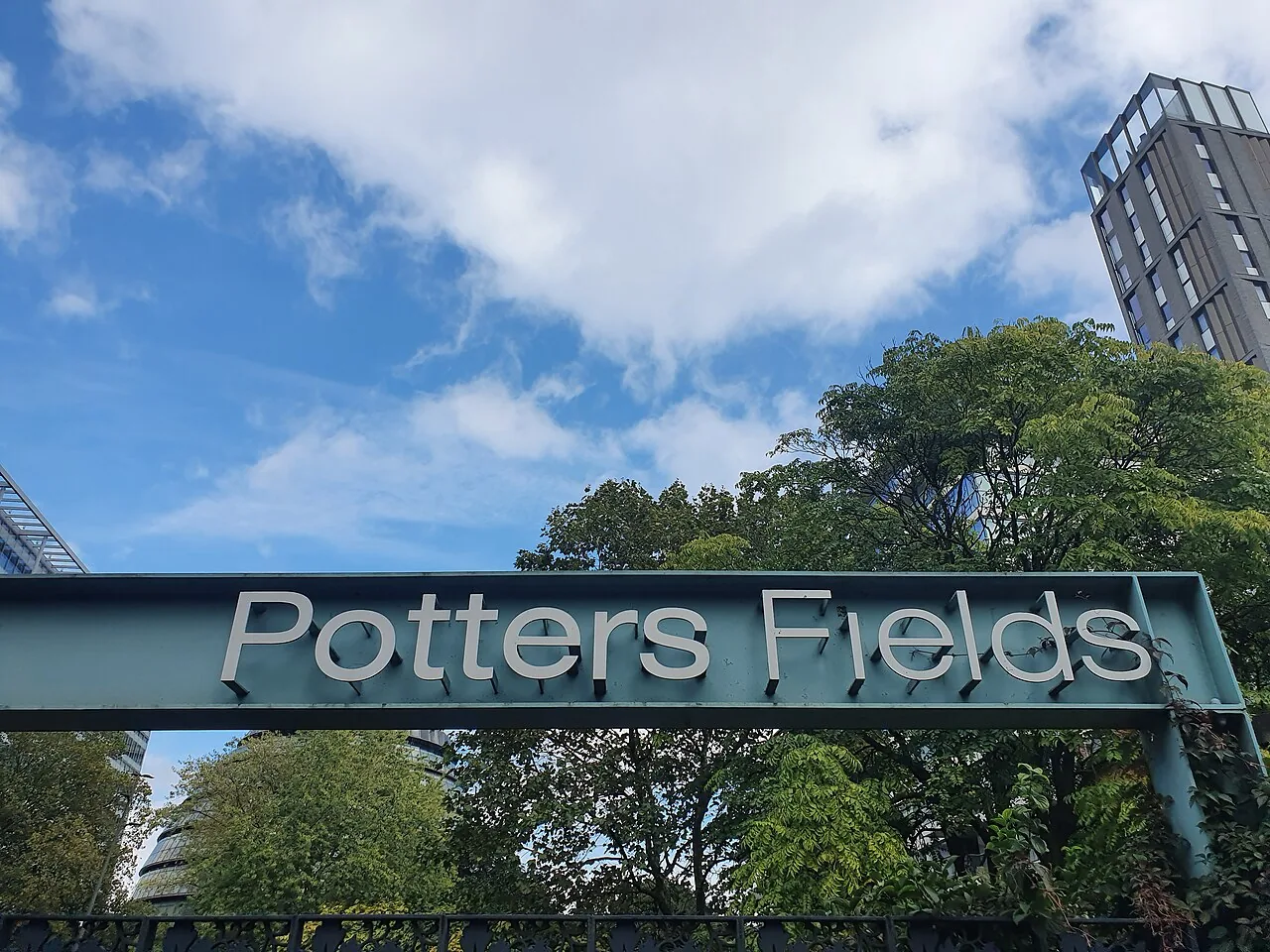 Potters Fields entrance sign above a path with planting and nearby buildings