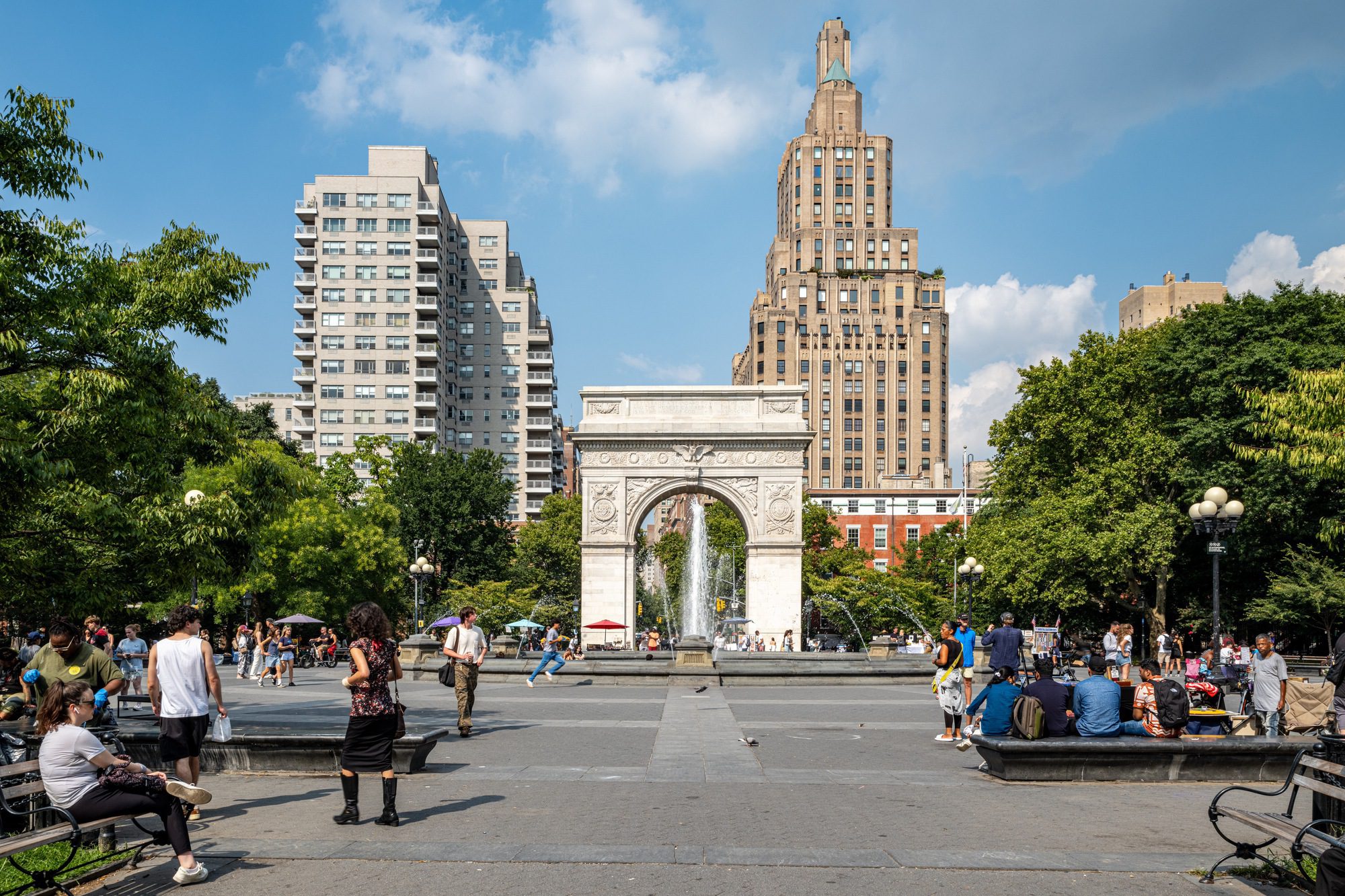 People gather in Washington Square Park surrounded by trees and city buildings